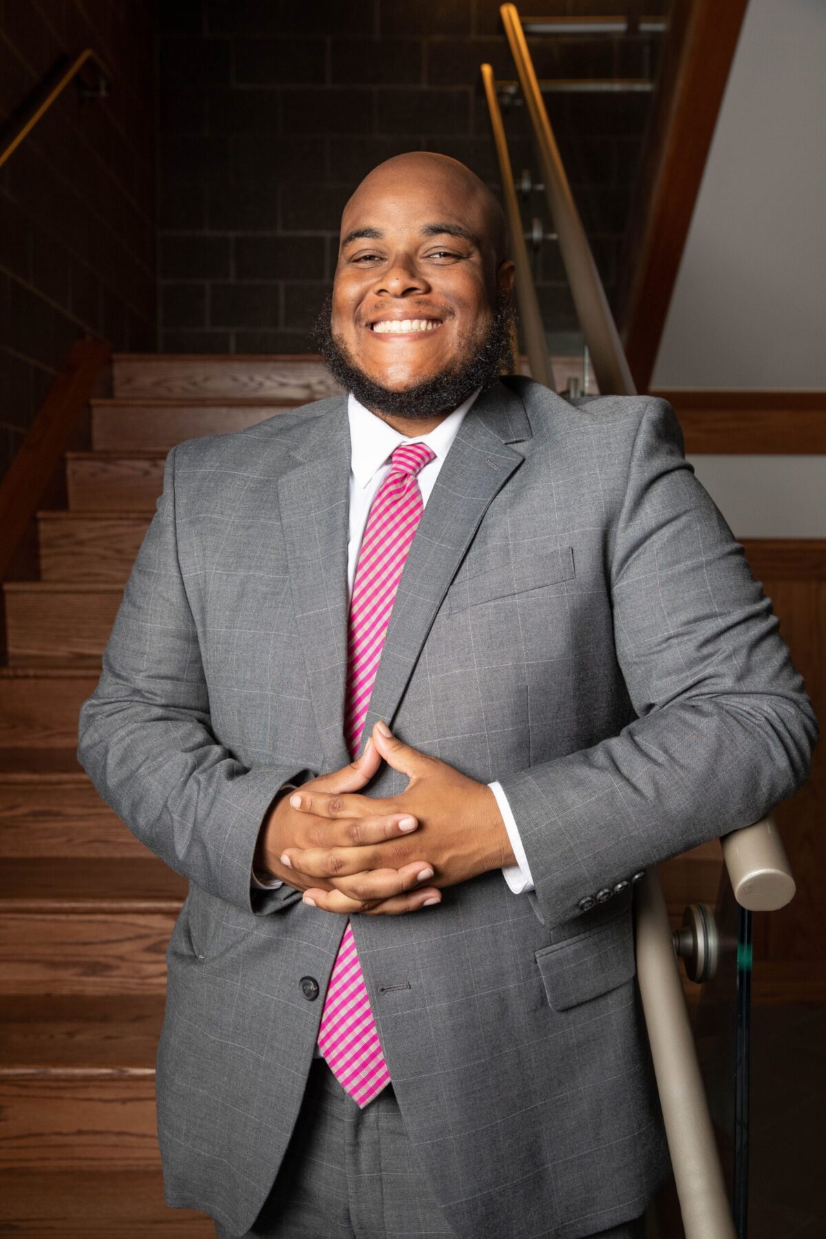 Headshot - Fidel E Benton, black man smiling in gray suit with pink tie